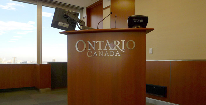Photo du podium fixe en bois comportant le logo des gouvernements de l’Ontario et du Canada dans la Salle de conference