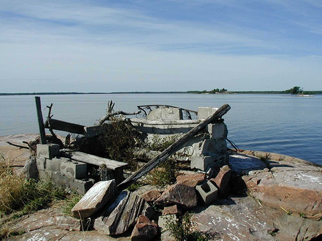 this photo shows an image of a Duck Blind constructed of wood and cement blocks on the shore.