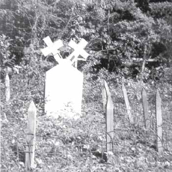 black and white photograph of a cemetery featuring a white grave marker with two crosses coming from the top.