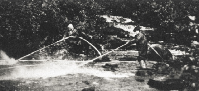 Black and white photo showing people using high-pressure fire hoses.
