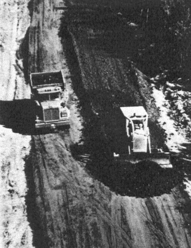 Black and white photo showing two trucks filling in a road.