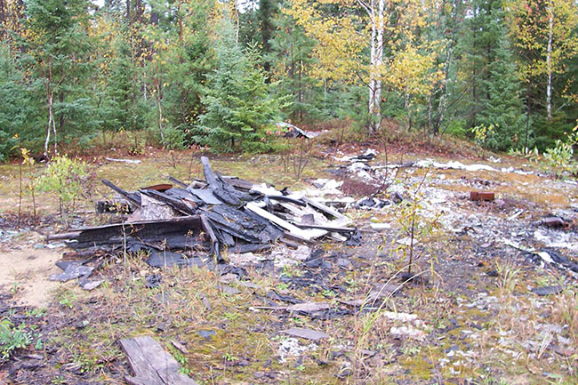 Photo shows that the old trapper’s cabin has been burned to the ground and a burned down cabin remains at the site.