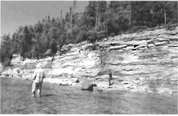 Thi sphoto shows two men on the shore and some trees on distance, Jacobsville Sandstone bluffs central-western shore of Ile Parisienne