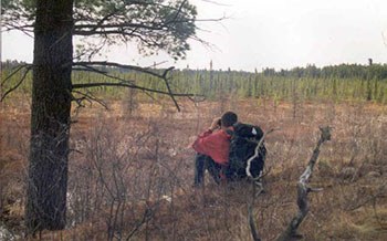 This photo shows an individualbeside a tree doing wildlife/bird viewing in the Loudon Basin Peatland.