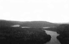 Black and white photo of a view from western boundary, looking southeast down arm of large
 upper unnamed lake in the Conservation Reserve’s southwest corner. Surrounded by black spruce dominant conifer, white birch pure, black spruce conifer mixed, white birch/Pj true mixed, black spruce mixedwood and Pj mixedwood forest communities.