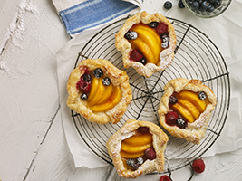 Peach and berry tarts on a wire cooling rack with a white cloth underneath 