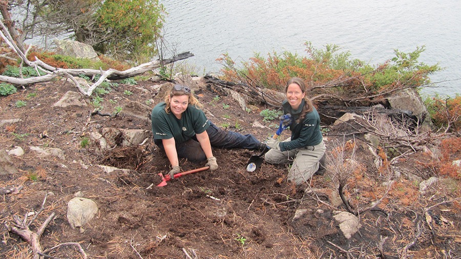 A photograph of two Parks Canada employees working on the bank of a river