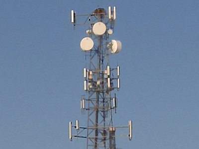 A collection of round and long, box-shaped structures mounted on top of a tower.