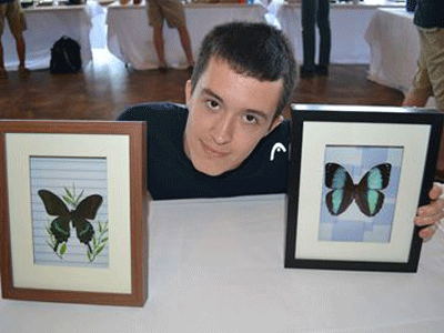 Photo of Glen Reavie, founder of Entostatic: Insect Taxidermy, holding two picture frames that showcase butterflies.
