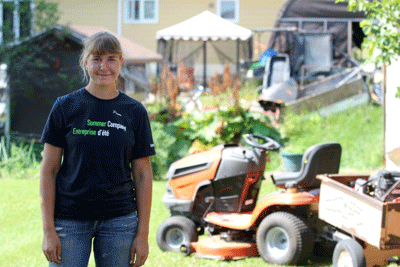 Photo of Anna Dalcin, founder of Anna’s Lawn Care, with a riding lawnmower in the background.