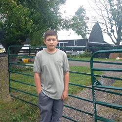 Photo of Spencer Douglas-Hill, founder of Right Hand Man Services, standing in front of a gate with a farm in the background.