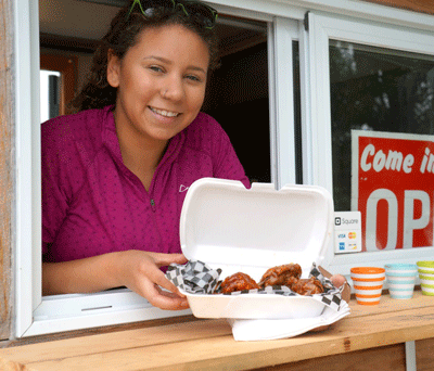 Photo of Cassie Wilson, founder of Cassie’s Southern Kitchen, holding a food container with chicken wings.
