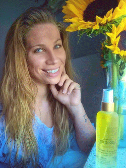 Photo of Charlee Johnston, founder of NakdBasics, pictured with one of her spray bottle products and an arrangement of sunflowers.