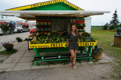 Photo of Emma Arnott, founder of Two Sisters Fruit & Vegetables, standing in front of her fruit and vegetable stand.