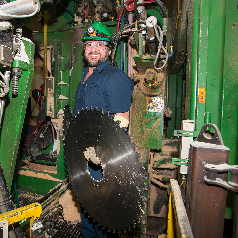 A person working in an industrial setting and holding a large saw blade.