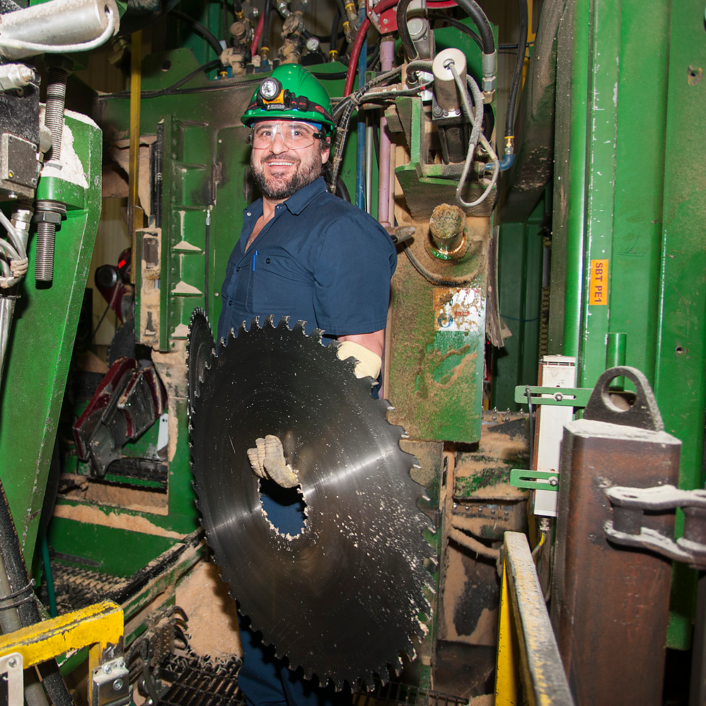 Une personne qui travaille en industrie et qui tient une grande lame de scie.