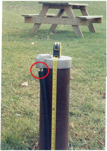 Figure 11-7 shows a drilled well with a tape measure on top of a well cap. An open hole exists between the well cap and the white electrical wires and black conduit (on left side of well casing). It is likely that the top of the black conduit has slid down from the well cap over time to create the opening at the well cap. The opening (circled) provides a pathway for foreign materials such as insects, rodent and snakes to access the well and contaminate the well water.