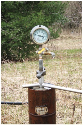 Figure 12-5 shows a flowing well pressure gauge device. It is made with an Ethylene Propylene Diene Monomer rubber packer which is sealed between two stainless steel plates at the bottom of the device. A steel rod with a tightening device and pressure gauge is installed to the packer. The packer is installed into the top of the well casing. Using the tightening rod, the steel plates squeeze the Ethylene Propylene Diene Monomer rubber to the sides of the well casing which pressurizes the water column. The pressure is detected by the device through the steel rod into the gauge. The gauge provides the artesian head pressure at the elevation of the gauge.