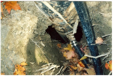 Figure 15-24 shows the outside of the well casing from ground level with a pitless adapter and horizontal waterline extending from the well. Also, the photograph shows a large opening on the outside of the well that will need to be filled.