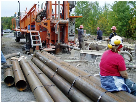 Figure 15-49 shows the casing of the drilled well extending just above the ground surface behind the drill rig. The drill rods are attached to the drill rig and extend down into the well casing.