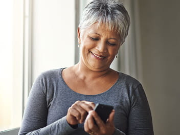 An older adult smiling and using a smartphone.