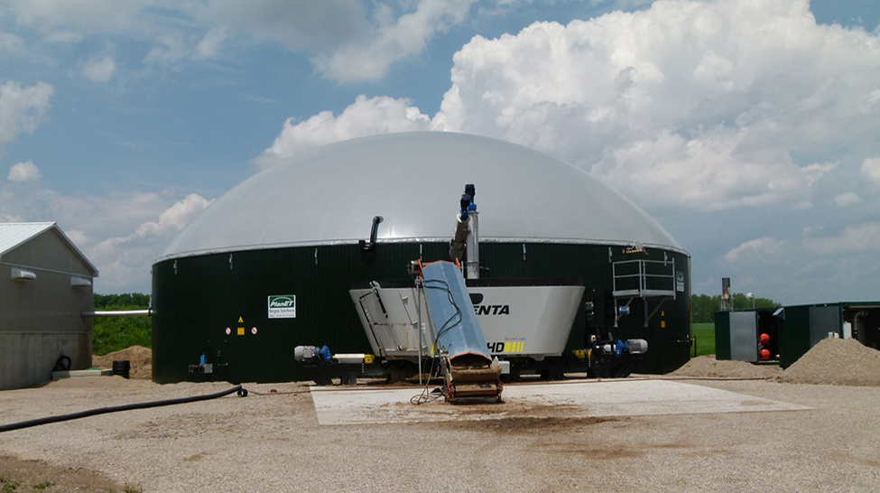 Exterior view of an anaerobic digester with auger shown in front to load feedstock into the digester.