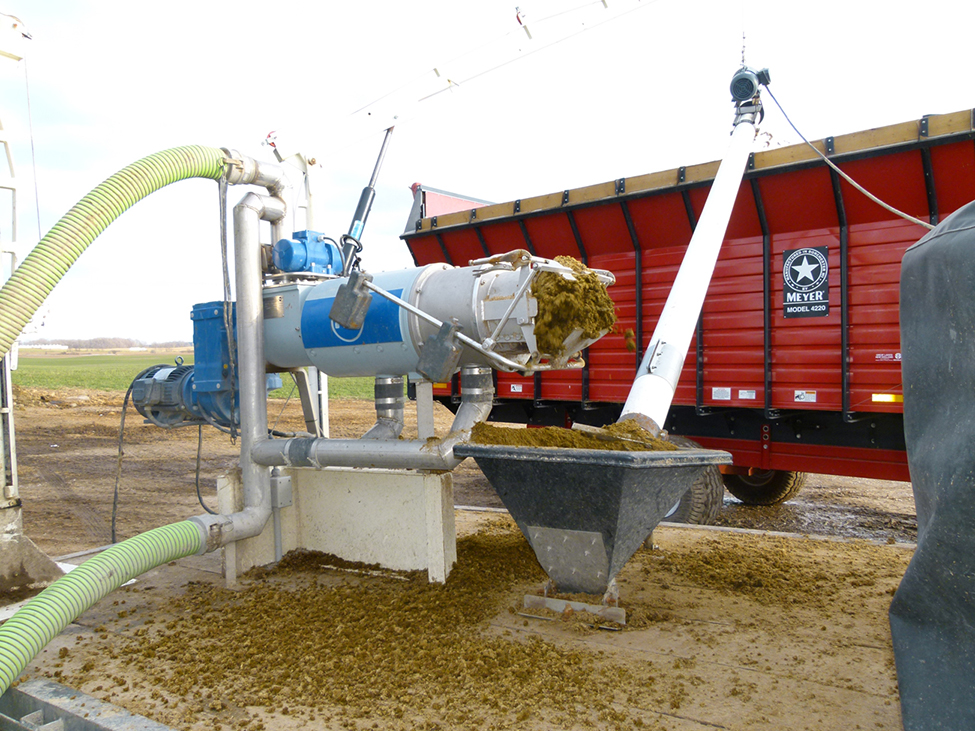 Screw-press separating solids from manure and emptying solids into a bin with auger moving solids into red trailer.