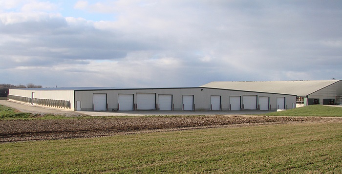 Very wide single-storey dairy barn with fans on left side and multiple roll-up doors on front.