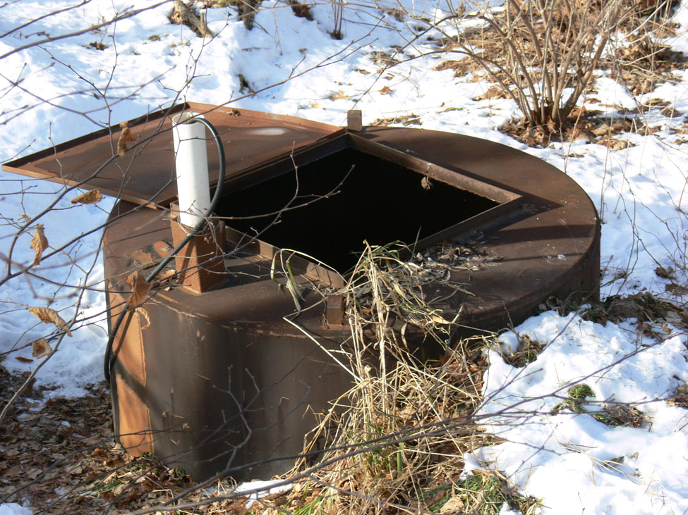 A disposal vessel, for small livestock, that is fully submerged in the ground. The hatch is open and there is a pipe for air circulation.