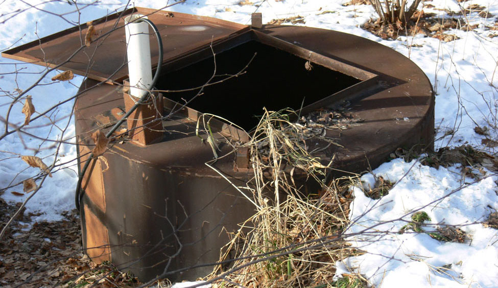 Photo prise durant l’hiver, à environ 2 m de distance d’un conteneur d’élimination cylindrique en acier dont le couvercle est grand ouvert. Le conteneur fait environ 2 m de diamètre.