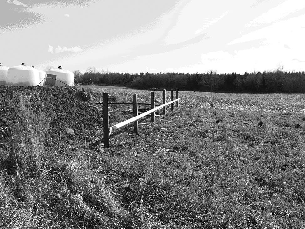 A photo of a distribution pipe, in a field, for a vegetated filter strip system. The pipe is located at the top of the vegetated filter strip, allowing the washwater to flow down the slope.