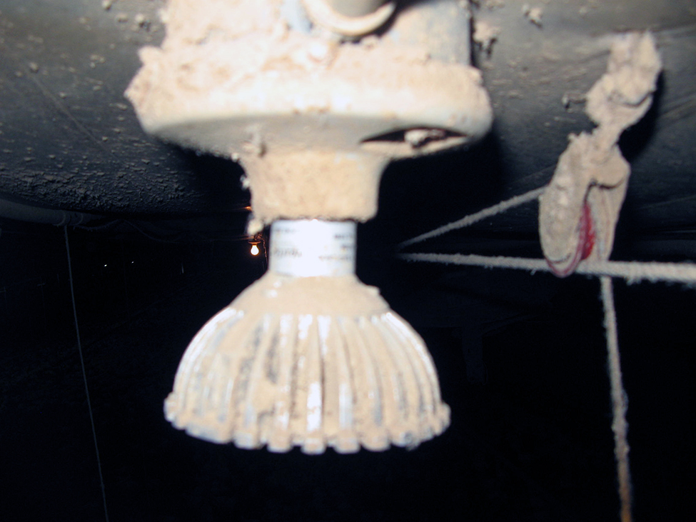 Photo showing a different model of a finned LED bulb, suspended from a ceiling, covered in a layer of dust.