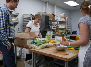 This is a picture of Marianne Katusin, Interim Director, Clinical Nutrition and Food Services and other foodservice staff in the kitchen at Oakville Trafalgar Memorial Hospital located in Oakville. The foodservices team is preparing meals using Ontario ingredients as part of their award-winning personalized meal delivery services for their hospital patients.