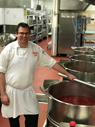 Andrew Bilyk, sous-chef aux services d'hôtellerie de l'Université de Guelph est debout à côté d'équipement de cuisine commercial préparant des repas pour le programme de livraison d'urgence à domicile de l'organisme The SEED.
