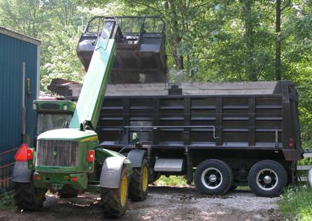 Photo d’un type de tracteur spécial avec un bras extensible et une grosse pelle qui dépose du fumier de cheval dans un camion à benne.