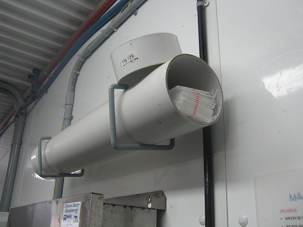 horizontal plastic tube mounted on the wall with the lid off showing milk filters inside