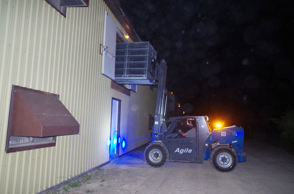 Forklift placing empty, 5-tier CM2A module into second floor of barn at night