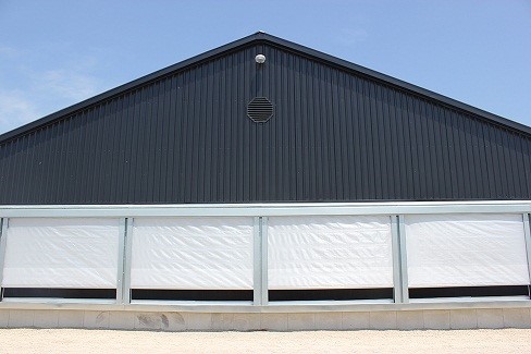 Picture of evaporative cooling pads with an exterior weather protection curtain (white curtain) that is partially closed.