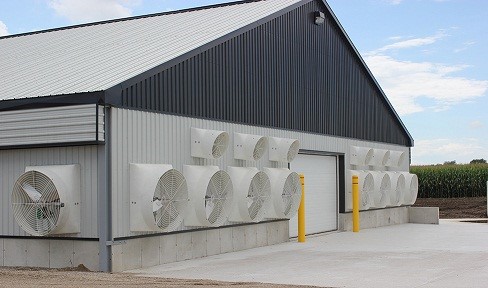 Picture of the end wall of a barn showing 9 large fans (48-inch diameter) and 6 small fans (24-inch diameter) mounted across the end of the building. These fans exhaust air from the barn to create the wind tunnel effect inside barn.