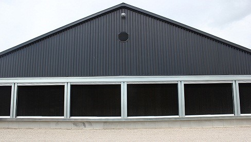 Picture of the tunnel inlet end of the barn with an evaporative cooling pad installed. Exterior covers have been pulled in to expose the black cooling pads.
