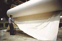 Picture of a man working in a paper mill, pulling on a large roll of paper.