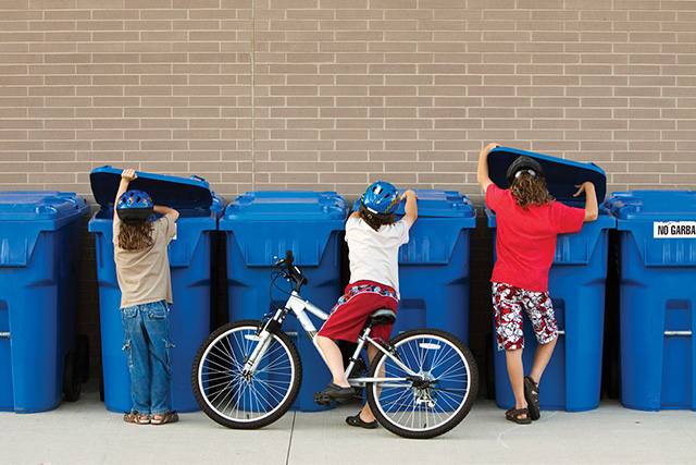 Photo of children looking in a row of recycling bins.